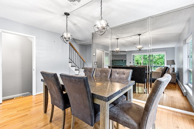 dining room with an inviting chandelier, visible vents, light wood-style floors, stairs, and a baseboard heating unit