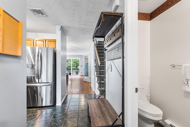 interior space featuring a baseboard heating unit, stainless steel refrigerator with ice dispenser, a textured ceiling, and visible vents
