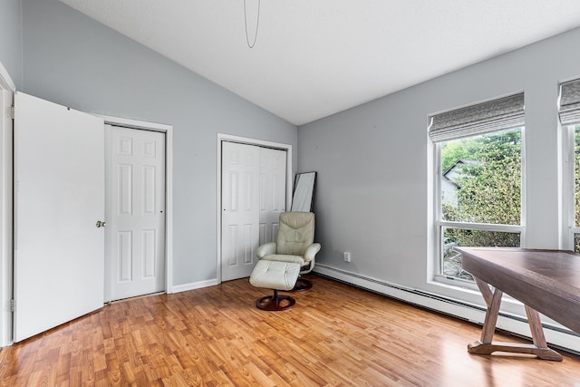 unfurnished room featuring light wood-style floors, a baseboard radiator, and vaulted ceiling