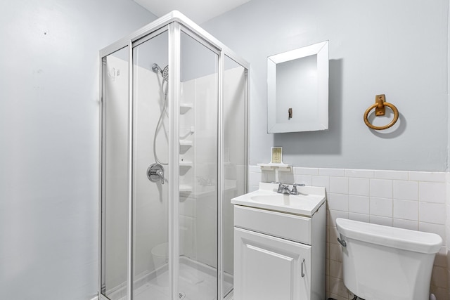 bathroom featuring vanity, wainscoting, toilet, tile walls, and a stall shower