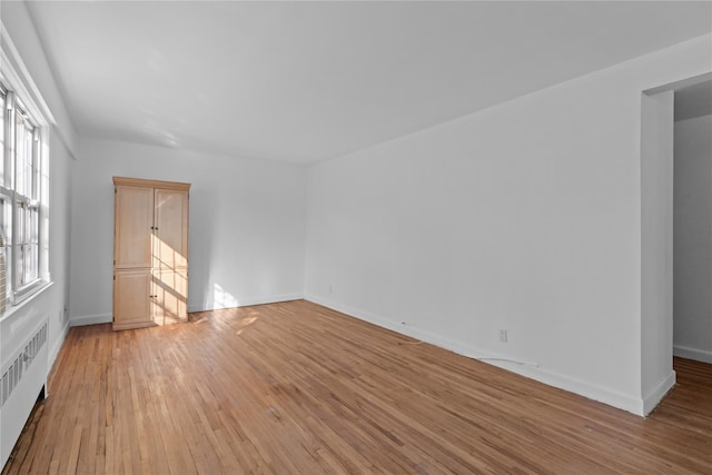 empty room with baseboards, light wood finished floors, and radiator heating unit