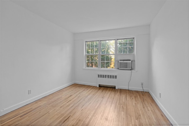 spare room featuring cooling unit, hardwood / wood-style flooring, baseboards, and radiator heating unit