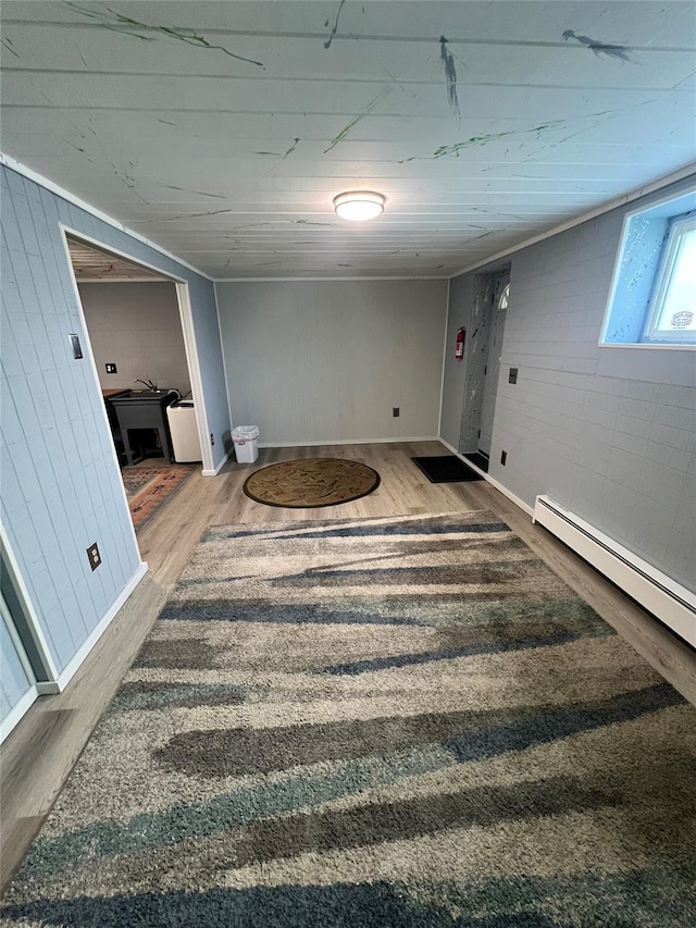 below grade area featuring wooden walls, baseboards, baseboard heating, and wood finished floors