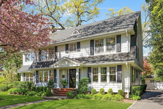colonial inspired home with roof with shingles, a front yard, and a chimney