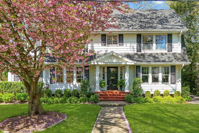 colonial-style house featuring a shingled roof and a front lawn