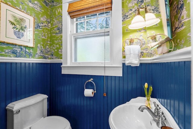 half bathroom featuring a sink, toilet, a wainscoted wall, and wallpapered walls