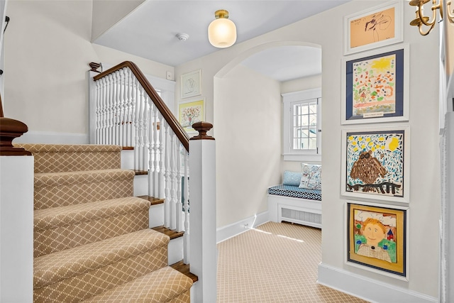 stairway featuring baseboards, arched walkways, and carpet flooring