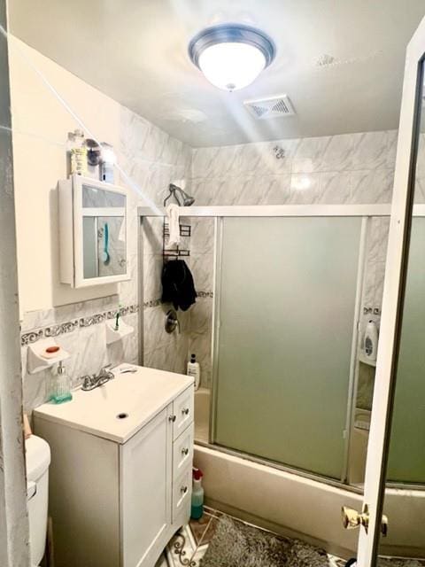 3231 Grace Ave, Bronx, NY 10469 - full bathroom with visible vents, vanity, toilet, tile walls, and bath / shower combo with glass door