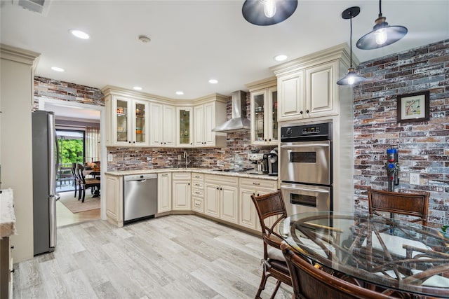 185 Old Pond Ct Unit 185, Jericho, NY 11753 - kitchen with cream cabinets, appliances with stainless steel finishes, wall chimney exhaust hood, light wood finished floors, and backsplash