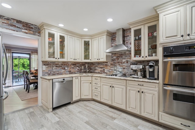 185 Old Pond Ct Unit 185, Jericho, NY 11753 - kitchen with appliances with stainless steel finishes, wall chimney exhaust hood, cream cabinetry, light wood-style flooring, and backsplash