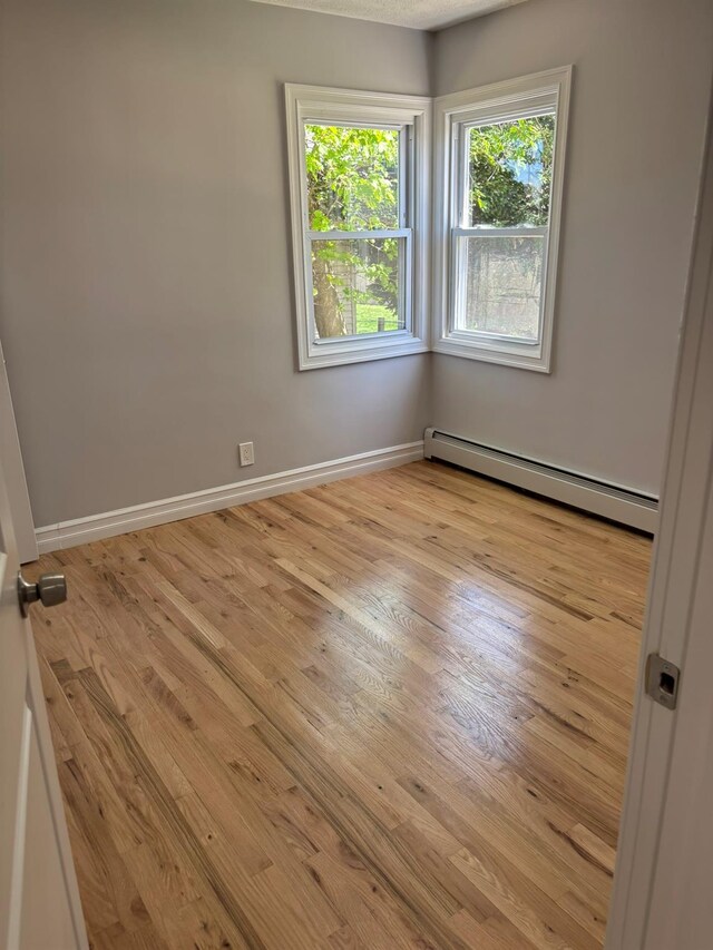 unfurnished room featuring a healthy amount of sunlight, baseboards, baseboard heating, and wood finished floors