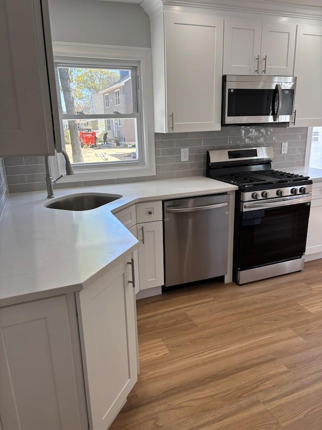 kitchen featuring appliances with stainless steel finishes, light wood-type flooring, a sink, light countertops, and white cabinets