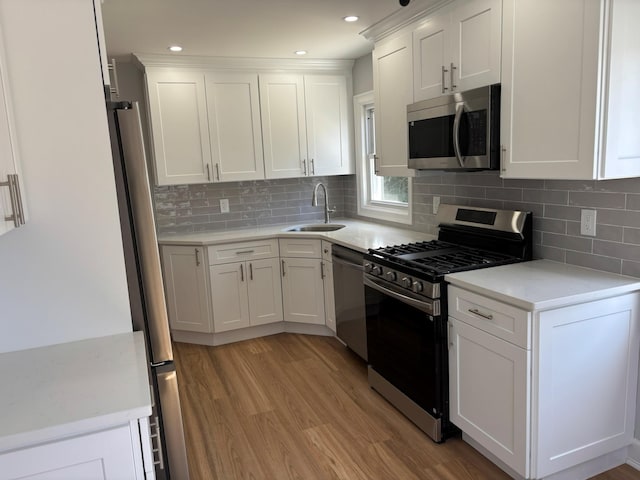 kitchen featuring appliances with stainless steel finishes, a sink, light wood-style floors, light countertops, and white cabinetry