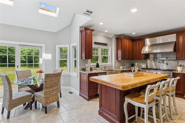 1465 Ackerly Pond Ln, Southold, NY 11971 - kitchen featuring wall chimney range hood, a kitchen island, recessed lighting, wooden counters, and a kitchen breakfast bar