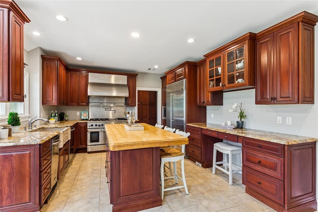 1465 Ackerly Pond Ln, Southold, NY 11971 - kitchen featuring wall chimney range hood, high quality appliances, reddish brown cabinets, butcher block countertops, and recessed lighting