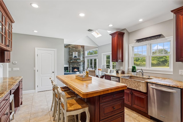 1465 Ackerly Pond Ln, Southold, NY 11971 - kitchen with stainless steel dishwasher, reddish brown cabinets, a stone fireplace, lofted ceiling, and a skylight