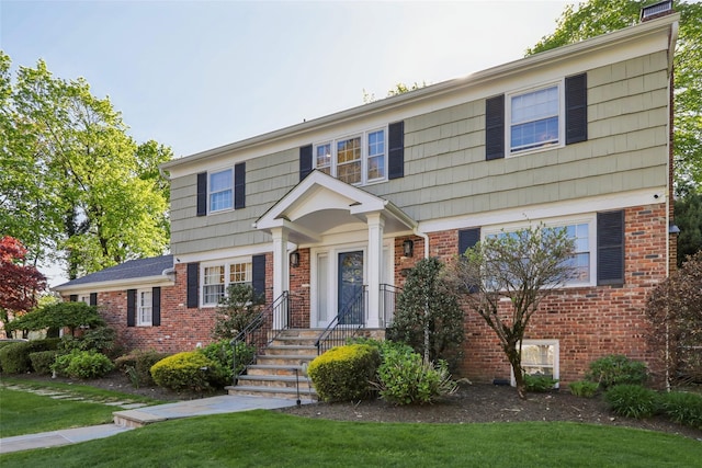 colonial-style house featuring brick siding and a front yard