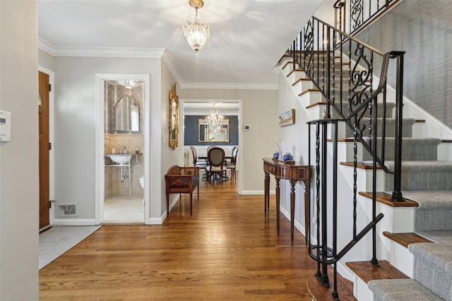 foyer with a chandelier, stairway, wood finished floors, ornamental molding, and baseboards
