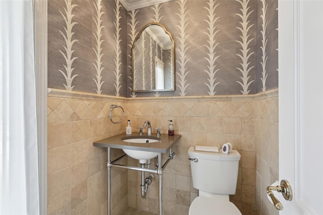 half bath with wallpapered walls, toilet, wainscoting, and tile walls