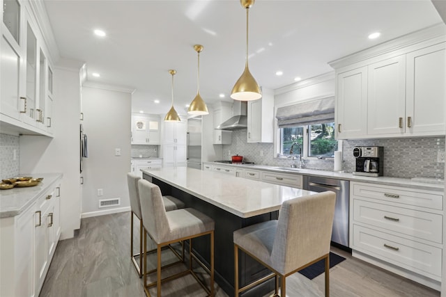 kitchen featuring stainless steel appliances, wall chimney range hood, backsplash, a kitchen island, and white cabinetry