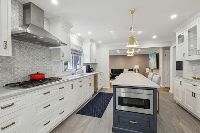kitchen featuring wall chimney exhaust hood, appliances with stainless steel finishes, a sink, open floor plan, and tasteful backsplash