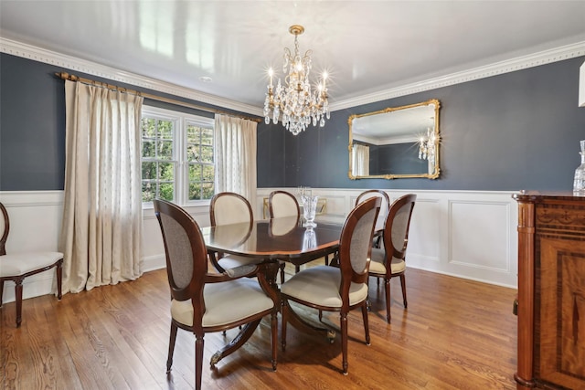 dining area with a chandelier, a wainscoted wall, wood finished floors, ornamental molding, and a decorative wall
