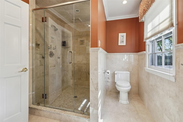bathroom with toilet, crown molding, a shower stall, wainscoting, and tile patterned floors
