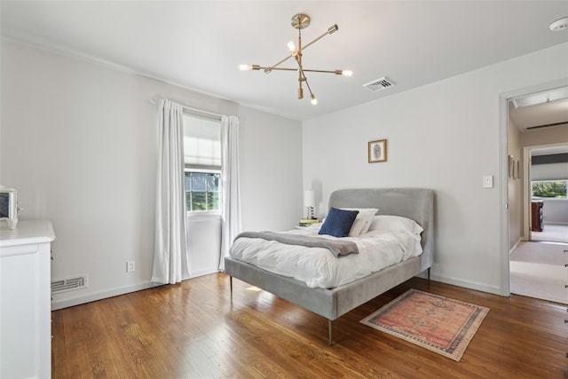 bedroom with wood finished floors, a chandelier, baseboards, and attic access