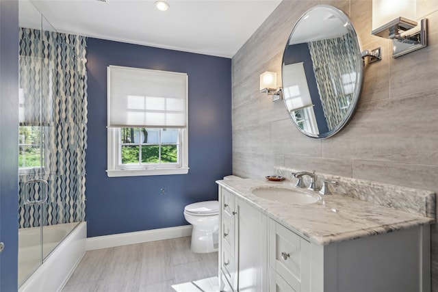 full bath with tile walls, toilet, vanity, baseboards, and an accent wall