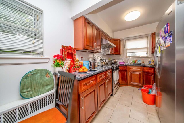 kitchen with tasteful backsplash, light tile patterned floors, freestanding refrigerator, range with gas stovetop, and under cabinet range hood