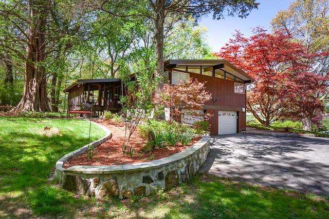 exterior space with a garage, a front lawn, aphalt driveway, a wooden deck, and a sunroom