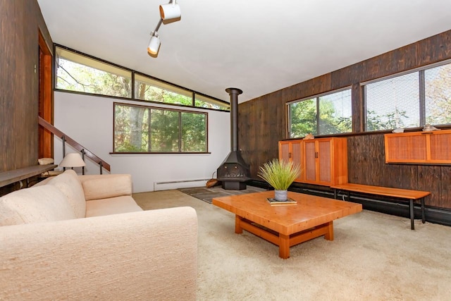 carpeted living room featuring a baseboard radiator, a wood stove, wood walls, and lofted ceiling