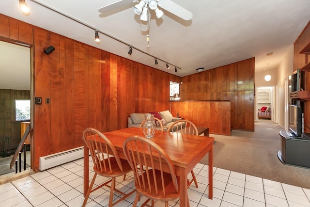 dining room with track lighting, wood walls, light tile patterned flooring, ceiling fan, and a baseboard heating unit