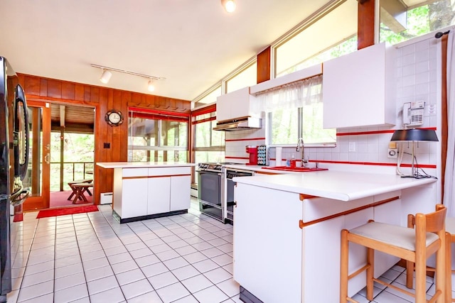 kitchen featuring track lighting, gas range oven, under cabinet range hood, a sink, and light tile patterned floors
