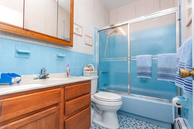 full bath featuring vanity, toilet, tile walls, baseboard heating, and bath / shower combo with glass door