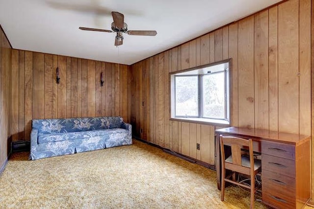 living area with ceiling fan, wood walls, and light colored carpet