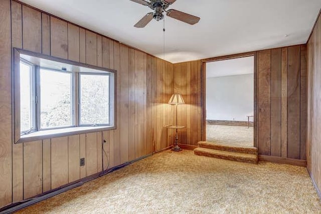 carpeted spare room featuring ceiling fan and wood walls