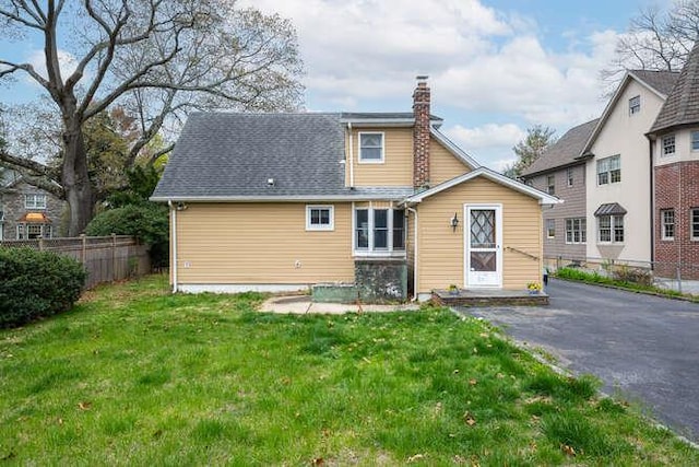 rear view of property with fence, a chimney, and a lawn