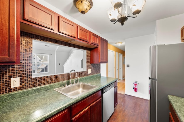 kitchen with decorative backsplash, dark countertops, dark wood-style floors, a sink, and appliances with stainless steel finishes