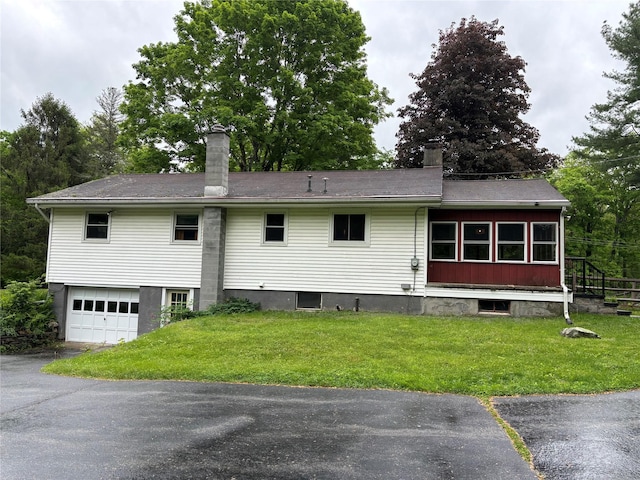 rear view of house featuring a chimney, a yard, an attached garage, and driveway