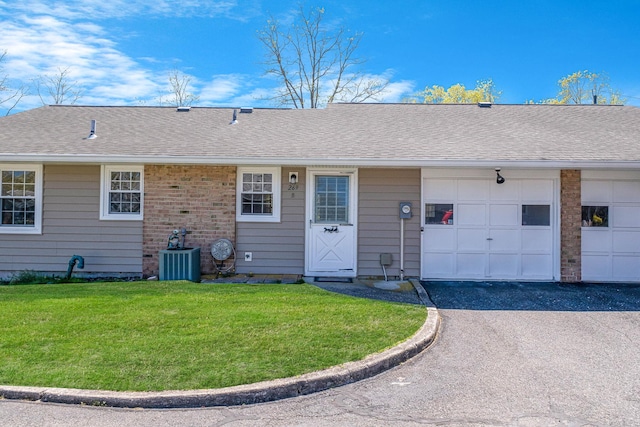 rear view of house with roof with shingles, aphalt driveway, a garage, central AC unit, and a lawn
