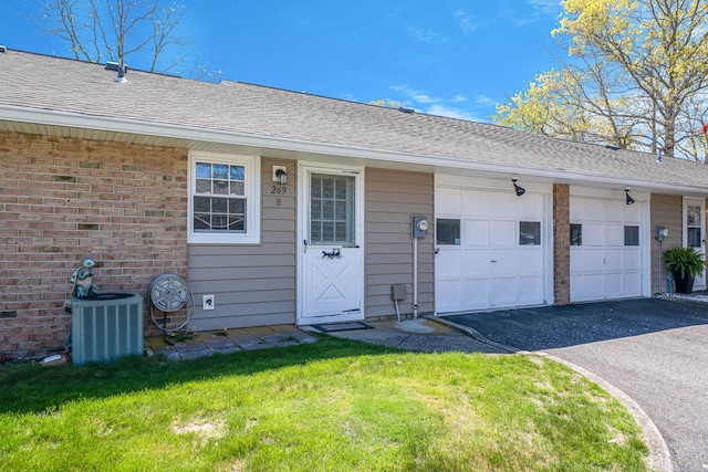 rear view of house featuring driveway, a garage, cooling unit, a yard, and a shingled roof