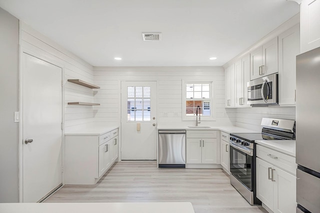 kitchen featuring white cabinets, appliances with stainless steel finishes, a sink, light countertops, and light wood-type flooring