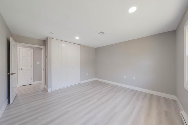unfurnished bedroom featuring a closet, baseboards, recessed lighting, a baseboard radiator, and light wood-style flooring