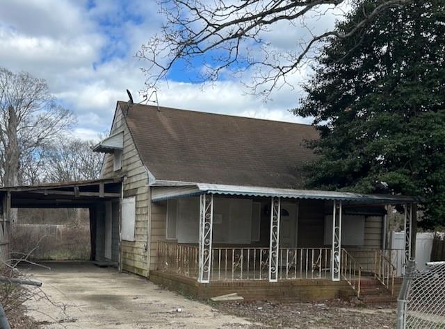 view of front facade with a porch, driveway, an attached carport, and roof with shingles
