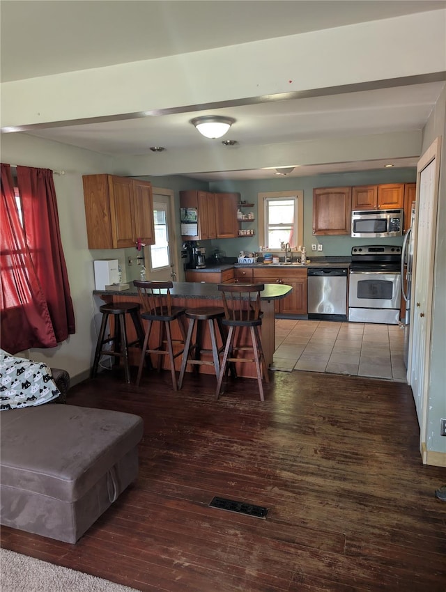 kitchen with stainless steel appliances, brown cabinetry, a sink, a peninsula, and a breakfast bar area