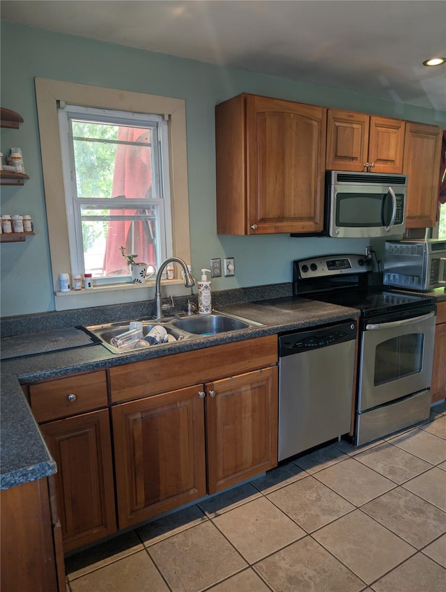 kitchen with stainless steel appliances, a sink, brown cabinetry, dark countertops, and recessed lighting