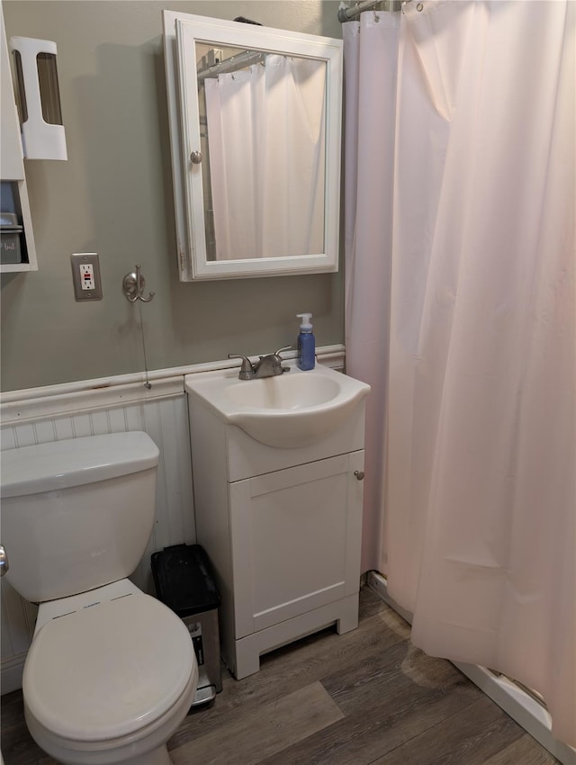 bathroom with wood finished floors, toilet, vanity, a wainscoted wall, and a shower with shower curtain