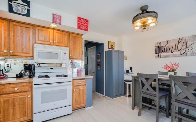 kitchen with light countertops, brown cabinets, light wood finished floors, and white appliances