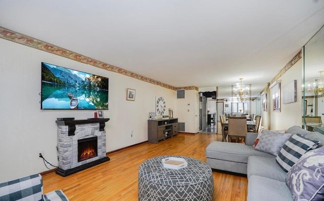 living area featuring a stone fireplace, baseboards, wood finished floors, and a notable chandelier